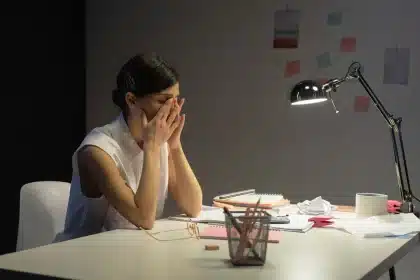 Personne épuisée assise à un bureau, tête dans les mains, environnement de travail fatigant