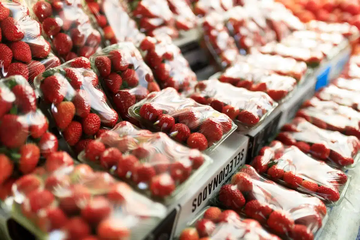 Fruits et légumes frais exposés sur un marché : fraises, concombres et petits pois.