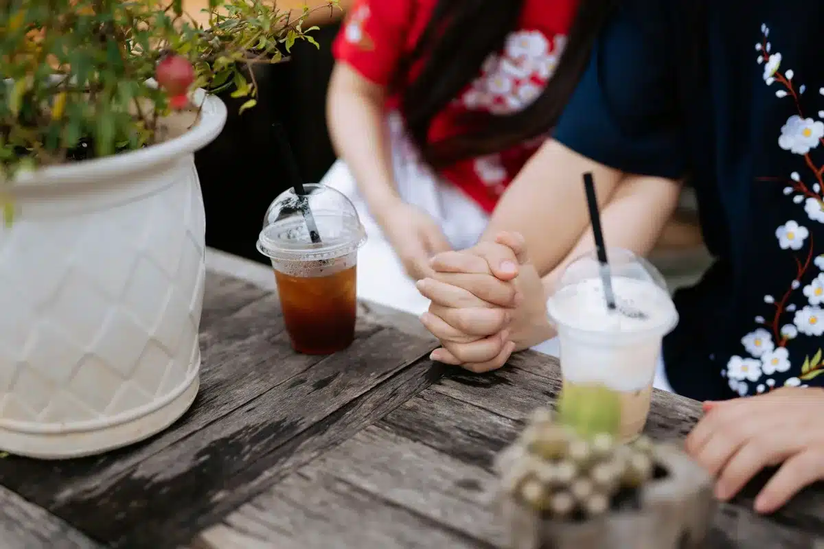Mains anonymes d'un couple autour d'une table ensoleillée avec carnet et tasse de thé