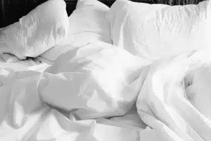 Chambre en plein jour avec draps légers en lin et percale, main touchant le tissu