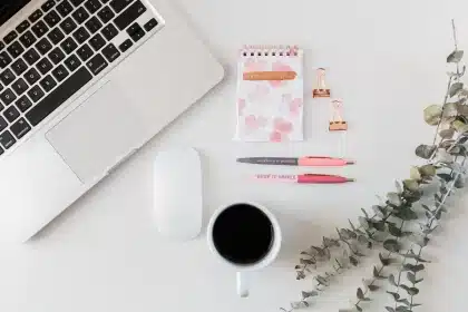 Deux mains tenant des mugs autour d'une table basse en journée, carnet et stylo à côté